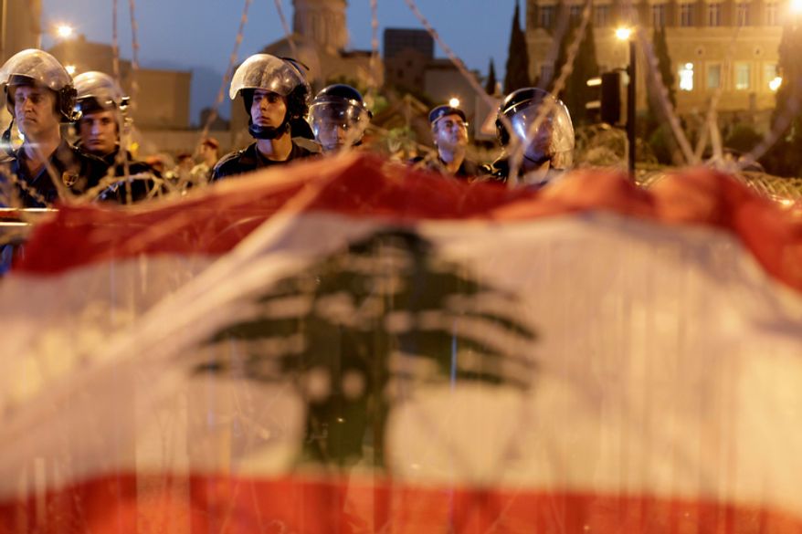 Lebanese riot police stand guard in front of the government palace behind a barbed wire barricade decorated with the national flag by anti-government protesters in downtown Beirut on Oct. 22, 2012. Lebanese troops launched a major security operation on Monday to open all roads and force gunmen off the streets, trying to contain an outburst of violence set off by the assassination of a top intelligence official who was a powerful opponent of Syria. Sectarian clashes killed at least five people. (Associated Press)