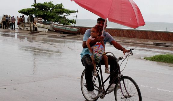 A man balances a child and umbrella on his bike as it rains during the approach of Hurricane Sandy in Manzanillo, Cuba, Wednesday, Oct. 24, 2012. Hurricane Sandy pounded Jamaica with heavy rain as it headed for landfall near the country&#39;s most populous city on a track that would carry it across the Caribbean island to Cuba, and a possible threat to Florida. (AP Photo/Franklin Reyes)