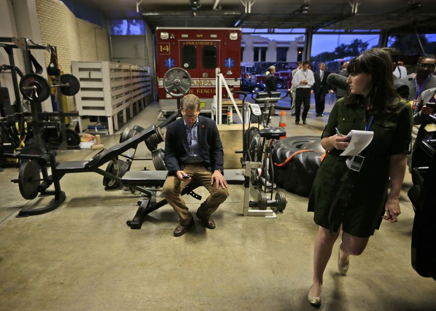 Tampa Bay Times reporter Katie Sanders (right) looks over toward White House spokesman Jay Carney (center), who takes a seat Oct. 25, 2012, in the workout area of Fire House No. 14. in Tampa, Fla., during President Obama's unannounced visit to meet with firefighters. Obama traveled to Florida for a campaign event nearby. (Associated Press)