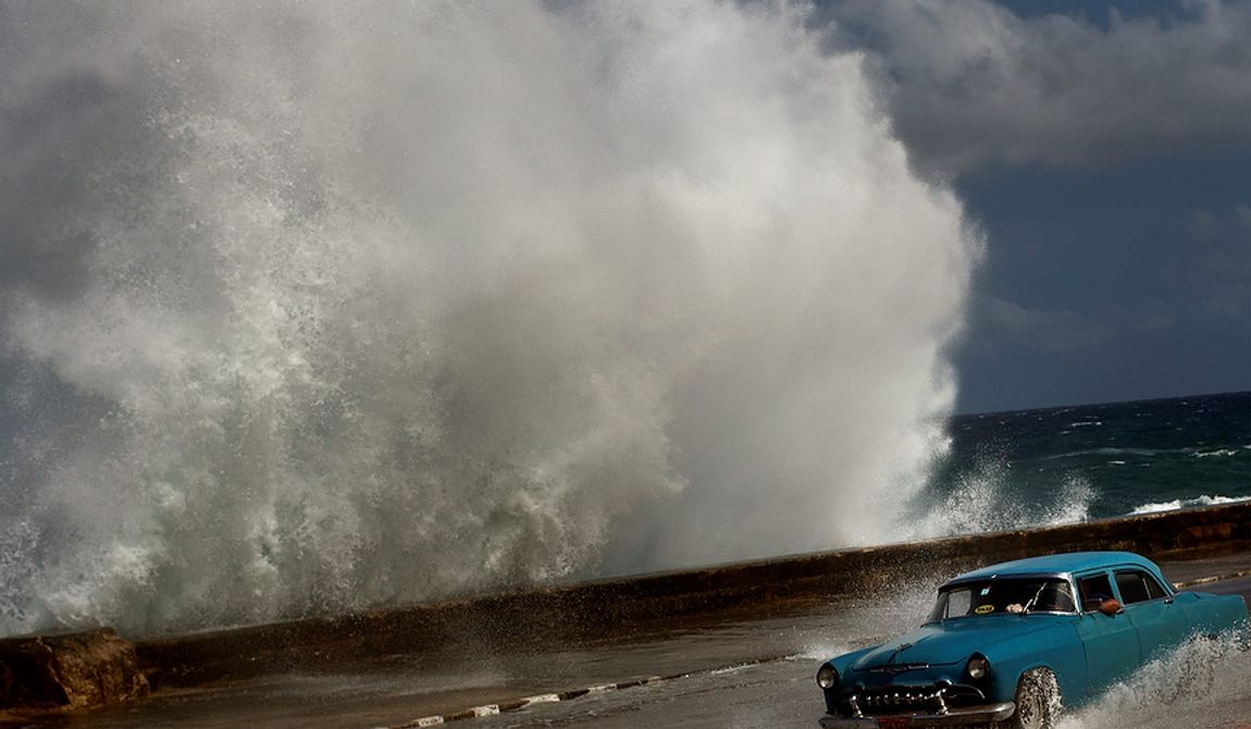 A driver maneuvers his classic American car along a wet road in Havana on Oct. 25, 2012, as a wave crashes against the car. Hurricane Sandy blasted across eastern Cuba as a potent Category 2 storm and headed for the Bahamas after causing at least two deaths in the Caribbean. (Associated Press)