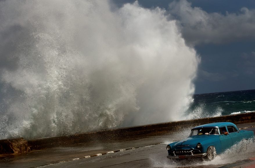 A driver maneuvers his classic American car along a wet road in Havana on Oct. 25, 2012, as a wave crashes against the car. Hurricane Sandy blasted across eastern Cuba as a potent Category 2 storm and headed for the Bahamas after causing at least two deaths in the Caribbean. (Associated Press)