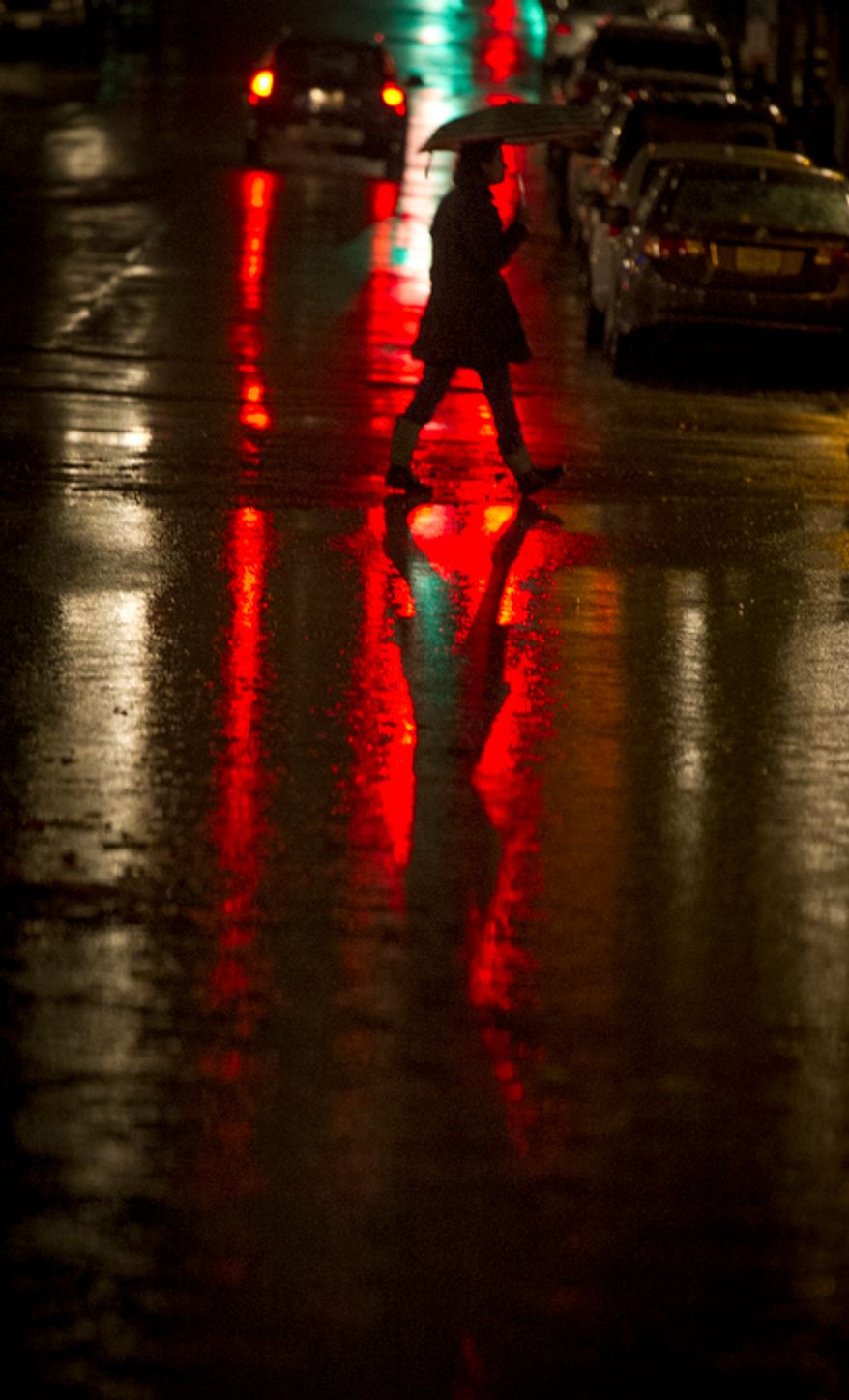 A woman crosses King Street under the shelter of an umbrella in a light rain during high tide, as a little flooding occurs along the waterfront in Old Town Alexandria, Va., Sunday, Oct. 28, 2012 while Hurricane Sandy makes it's way north along the Atlantic coast. (Rod Lamkey Jr./The Washington Times)