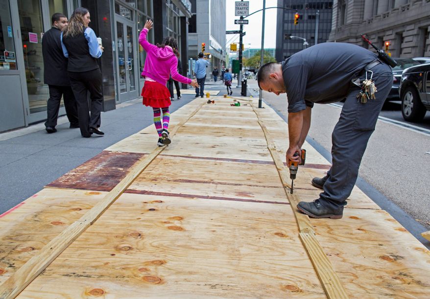 A maintenance worker named Vitto attaches plywood to a sidewalk grate at the 2 Broadway building of Lower Manhattan in New York, Sunday, Oct. 28, 2012, as a child walking by takes advantage of the temporary structure. Areas along the Northeast Coast are preparing for the arrival of Hurricane Sandy and a possible flooding storm surge. (AP Photo/Craig Ruttle)