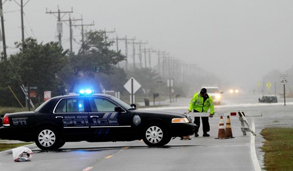 A police officer sets up a road block on South Oregon Inlet Road as water from Hurricane Sandy covers the road in Nags Head, N.C. (AP Photo/Gerry Broome)