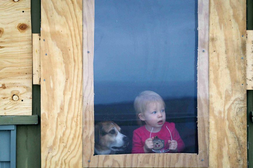 One-year-old Ever Long and her dog, Bailey, peek out the back door of their boarded house for the coming storm as some prepare for the approaching Hurricane Sandy, in Bay View Beach, Del. (AP Photo/The Wilmington News-Journal, Suchat Pederson)