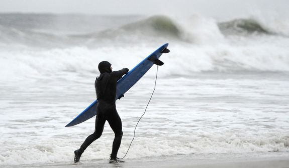 A surfer holds tight to his board against the strong winds and high surf of the Atlantic Ocean before the arrival of Hurricane Sandy on Sunday, Oct., 28, 2012, in Long Beach, N.Y.  (AP Photo/Kathy Kmonicek)