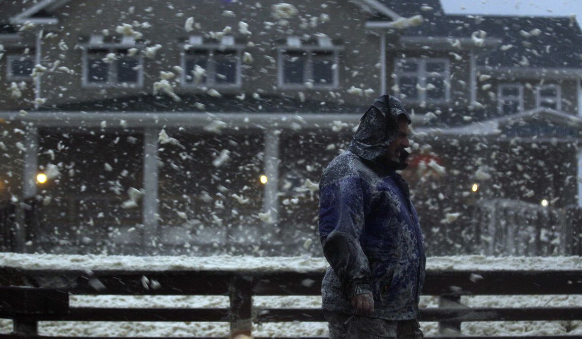 High winds blow sea foam into the air as a pedestrian crosses Jeanette&#x27;s Pier in Nags Head, N.C., on Sunday, Oct. 28, 2012, as wind and rain from Hurricane Sandy move into the area. (AP Photo/Gerry Broome)