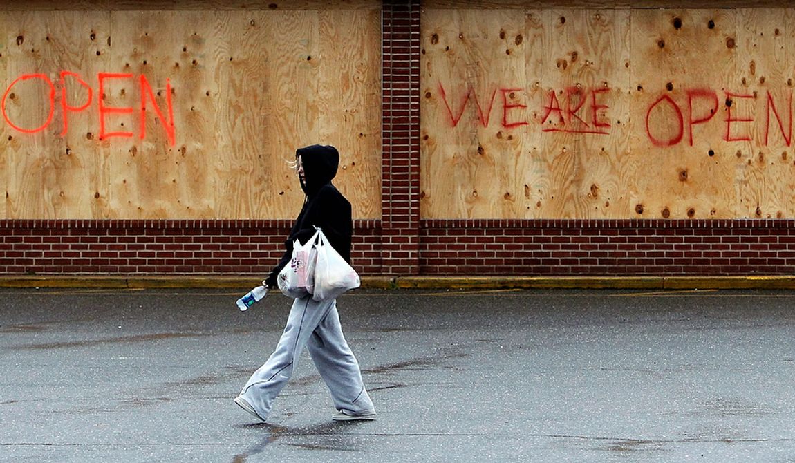 A woman carries bags back to her car after visiting a grocery store that is open for business despite being boarded up in advance of superstorm Sandy on Monday, Oct. 29, 2012, in Sayville, N.Y. Hurricane Sandy continued on its path Monday, forcing the shutdown of mass transit, schools and financial markets; sending coastal residents fleeing; and threatening a dangerous mix of high winds and soaking rain. (AP Photo/Jason DeCrow)