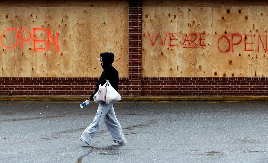 A woman carries bags back to her car after visiting a grocery store that is open for business despite being boarded up in advance of superstorm Sandy on Monday, Oct. 29, 2012, in Sayville, N.Y. Hurricane Sandy continued on its path Monday, forcing the shutdown of mass transit, schools and financial markets; sending coastal residents fleeing; and threatening a dangerous mix of high winds and soaking rain. (AP Photo/Jason DeCrow)