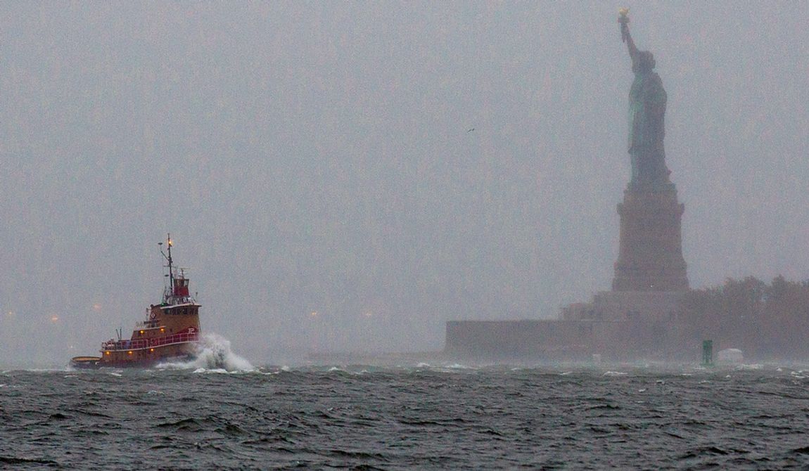 Waves crash over the bow of a tugboat as it passes near the Statue of Liberty in New York on Monday, Oct. 29, 2012, as rough water as the result of Hurricane Sandy churned the waters of New York Harbor. Hurricane Sandy continued on its path Monday, forcing the shutdown of mass transit, schools and financial markets; sending coastal residents fleeing; and threatening a dangerous mix of high winds and soaking rain. (AP Photo/Craig Ruttle)