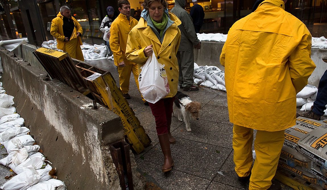 A pedestrian walks her dog through a working crew as they stack sandbags beside concrete barriers to protect buildings near the World Financial Center in anticipation of massive flooding on Monday, Oct. 29, 2012, in New York. Hurricane Sandy bore down on the Eastern Seaboard&#x27;s largest cities Monday, forcing the shutdown of mass transit, schools and financial markets; sending coastal residents fleeing; and threatening a dangerous mix of high winds, soaking rain and a seawater surge of anywhere from 6 to 11 feet. (AP Photo/John Minchillo)