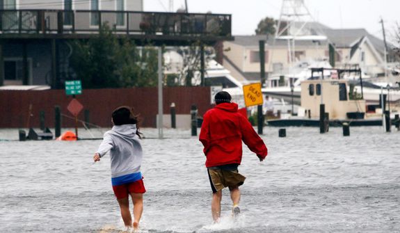 People run through a flooded street as Hurricane Sandy approaches, Monday, Oct. 29, 2012, in Lindenhurst, N.Y. Hurricane Sandy continued on its path Monday, as the storm forced the shutdown of mass transit, schools and financial markets, sending coastal residents fleeing, and threatening a dangerous mix of high winds and soaking rain. (AP Photo/Jason DeCrow)