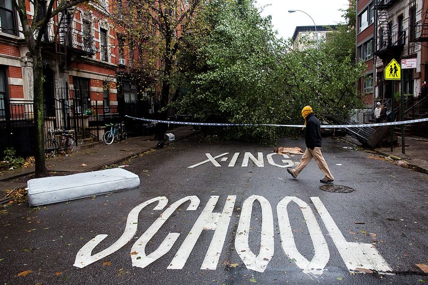 A pedestrian passes a fallen tree on East 7th Street in Manhattan's Lower East Side neighborhood, Tuesday, Oct. 30, 2012, in New York. New York City awakened Tuesday to a flooded subway system, shuttered financial markets and hundreds of thousands of people without power a day after a wall of seawater and high winds slammed into the city, destroying buildings and flooding tunnels. (AP Photo/ John Minchillo)
