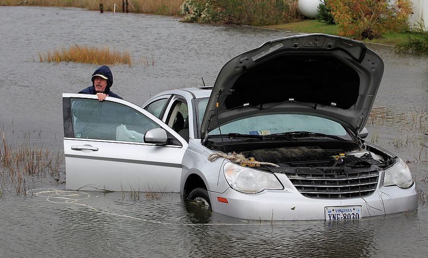 Glenn Heartley works on his car in a creek in Chincoteague, Va., Tuesday, Oct. 30, 2012. Heartley and his wife were swept off the road into a shallow creek when superstorm Sandy struck the area Monday. (AP Photo/Steve Helber)