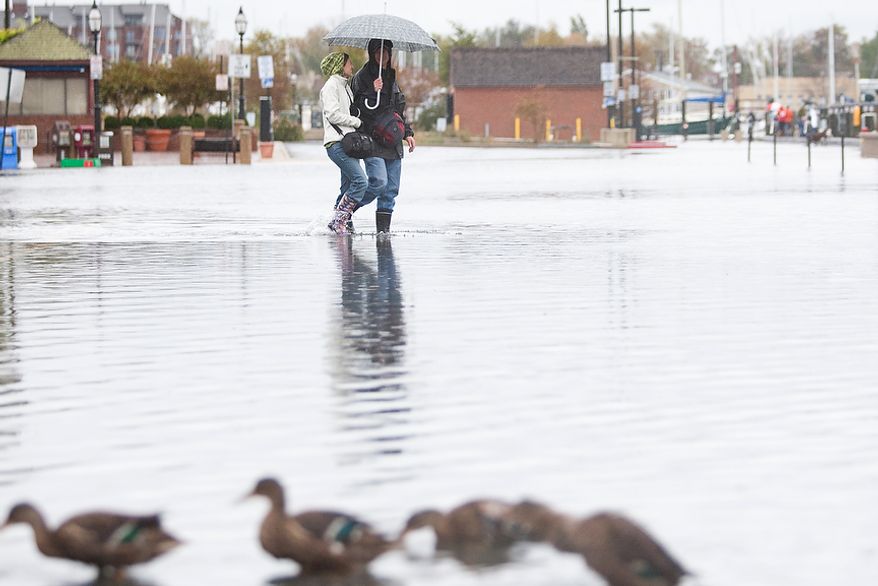 Sofie Lamartin, 22, from Annapolis, Md., left, walks with Erik Dronberger, 27, from Annapolis Md., walks though flooded Dock St., Annapolis Md., Tuesday, Oct. 30, 2012. The storm left early a foot and half of water along Dock St. but the stores are more worried about the tide which rises at 5:45pm and could bring another two feet of water. (Craig Bisacre/The Washington Times)