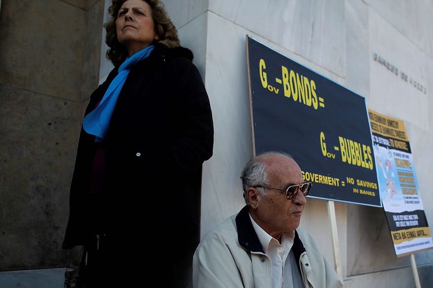 Greek bond holders stand at the entrance of Greece's central bank during a protest, in Athens Wednesday, Oct. 31 2012. Greece's two main labor unions covering civil servants and the private sector have called a 48-hour strike to protest austerity measures due to be voted on next week. The strike call came as the finance minister submitted an amended 2013 budget that raised the country's debt and deficit forecasts for next year. (AP Photo/Kostas Tsironis)