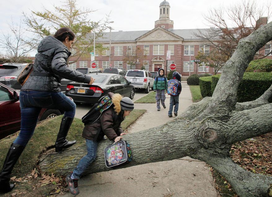 A woman and her son scramble over a tree toppled by Superstorm Sandy as she accompanies him to Public School 195 (background) in the Manhattan Beach neighborhood of Brooklyn in New York on Monday. Monday was the first day of public school for New York City students after the storm of a week ago. The woman declined to provide their names. Fewer than 50 schools throughout the five boroughs remained closed because of structural damage and fewer than 20 were without power. (Associated Press)
