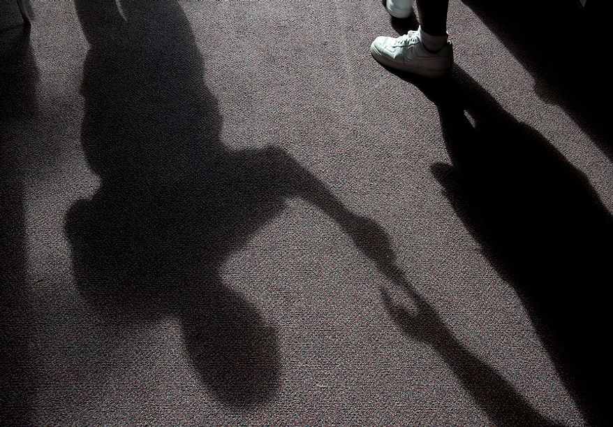 The shadow of Robert R. Black (left), a voter assistant clerk, is seen as he hands a "I Voted Today" sticker to a voter at Judiciary Square in Washington on Wednesday, Oct. 24, 2012. According to site officials, some 2,400 voters had voted here since Monday, when the early voting opened. (Barbara L. Salisbury/The Washington Times)