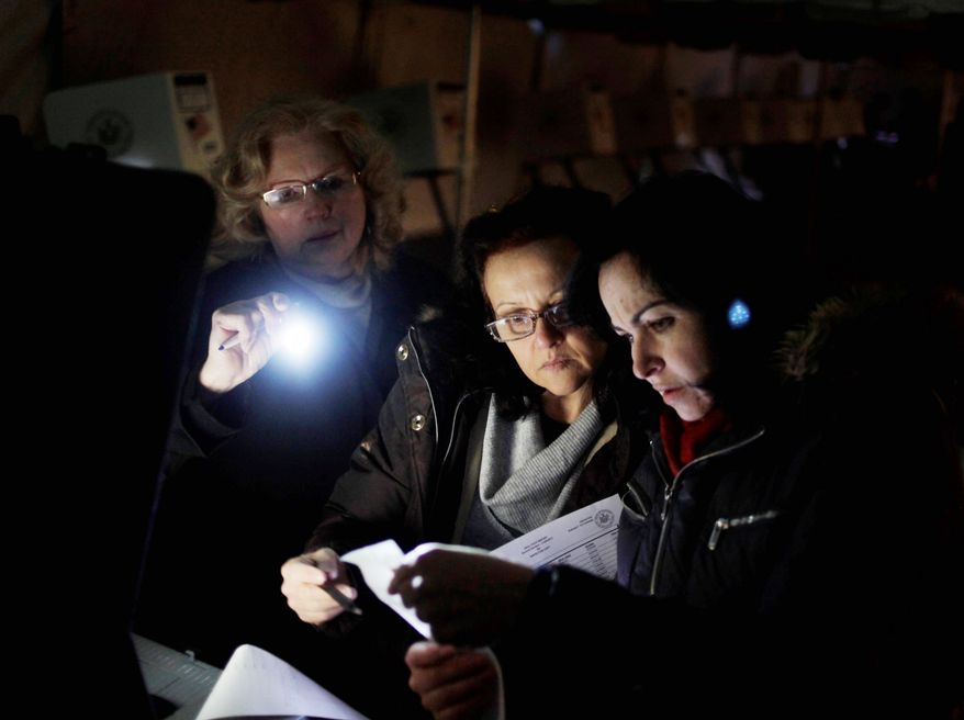 Poll workers Eva Prenga (right), Roxanne Blancero (center) and Carole Sevchuk try to start an optical-scanner voting machine in the cold and dark at a polling station in a tent in the Midland Beach section of Staten Island, N.Y. on Tuesday morning. The original polling site, a school, was damaged by the storm last week. (Associated Press)