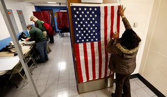 ** FILE ** Evelyn Dennis hangs a U.S. flag as election workers set up voting booths at Memorial Elementary School in Little Ferry, N.J., on Nov. 6, 2012. (Associated Press)