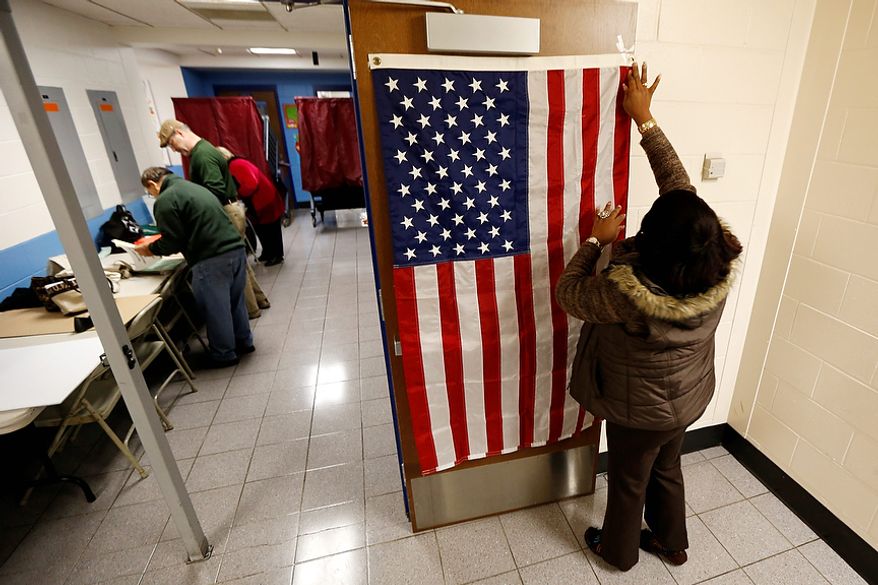 ** FILE ** Evelyn Dennis hangs a U.S. flag as election workers set up voting booths at Memorial Elementary School in Little Ferry, N.J., on Nov. 6, 2012. (Associated Press)