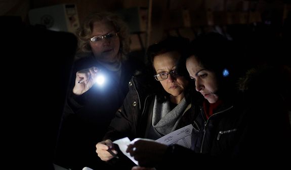 Poll workers (from right) Eva Prenga, Roxanne Blancero and Carole Sevchuk try to start an optical scanner voting machine in the cold and dark at a polling station in a tent in the Midland Beach section of Staten Island in New York on Tuesday, Nov. 6, 2012. The original polling site, a school, was damaged by superstorm Sandy. (AP Photo/Seth Wenig)