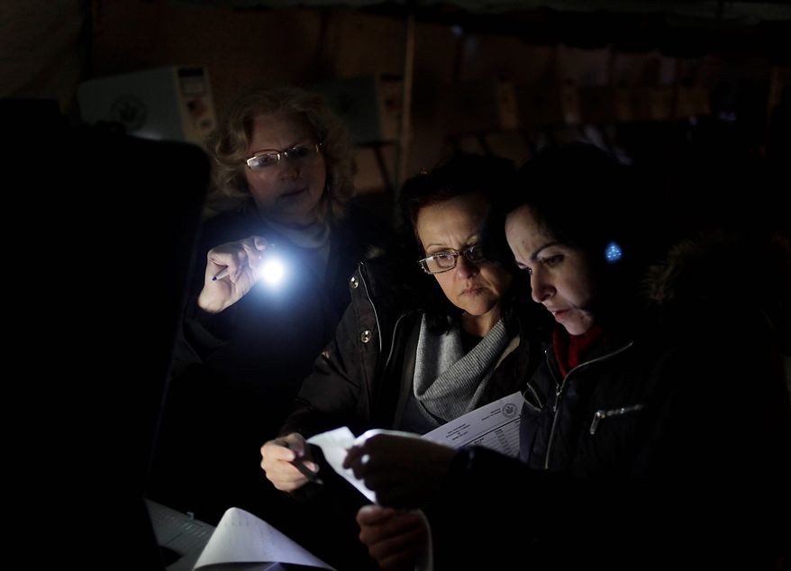Poll workers (from right) Eva Prenga, Roxanne Blancero and Carole Sevchuk try to start an optical scanner voting machine in the cold and dark at a polling station in a tent in the Midland Beach section of Staten Island in New York on Tuesday, Nov. 6, 2012. The original polling site, a school, was damaged by superstorm Sandy. (AP Photo/Seth Wenig)