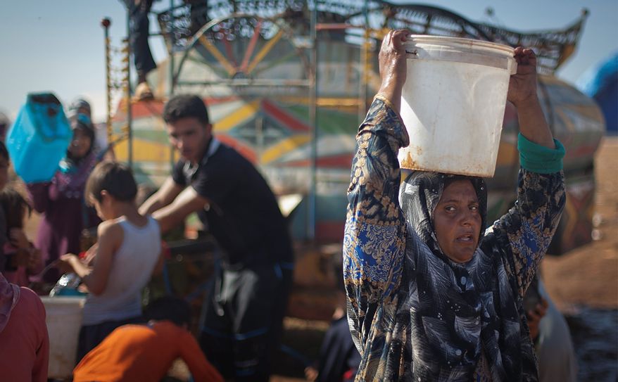 A Syrian woman who fled from the violence in her village carries a water bucket on her head Nov. 7, 2012, at a displacement camp in the Syrian village of Atma, near the Turkish border. (Associated Press)