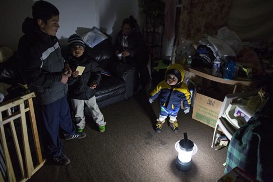 Living through another night of possibly freezing temperatures, Michael Pineda, 15 months old, stands bundled up near a battery-operated lantern in his home without power or heat in the Rockaway Park neighborhood in the Queens borough of New York, Thursday, Nov. 8, 2012, in the wake of Superstorm Sandy. From left is his brother Mario Pineda, 12, Walter Rivera, 5, and center in deep shadow is their mother Fatima Pineda. (AP Photo/Craig Ruttle)