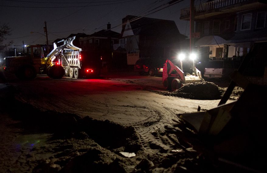 **FILE** A front loader works to remove sand and debris Nov. 11, 2012, as night falls on the Rockaway neighborhood in the Queens borough of New York in the wake of Superstorm Sandy. (Associated Press)