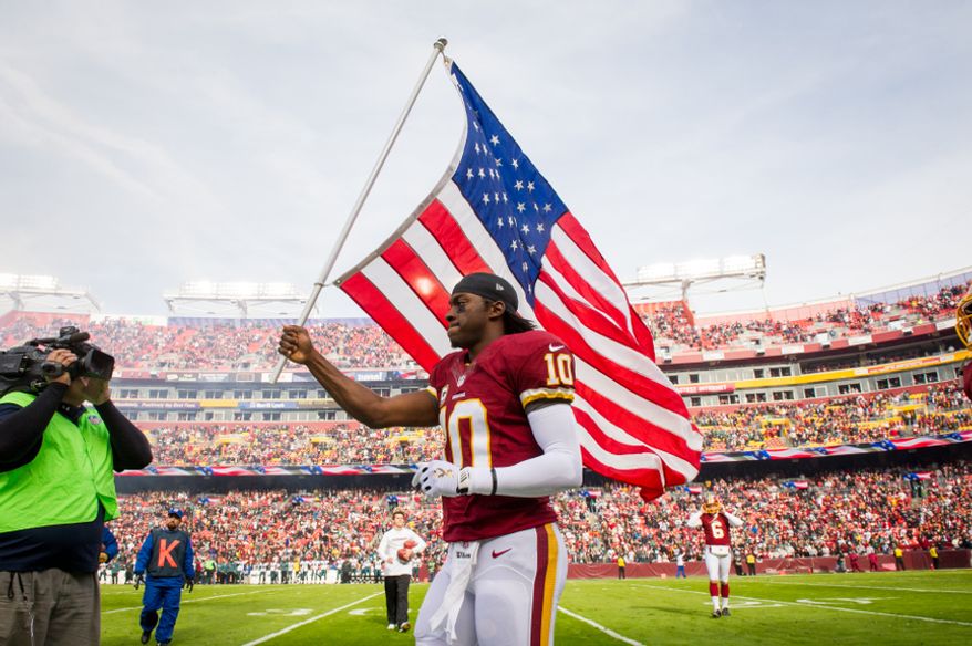 Washington Redskins quarterback Robert Griffin III (10) carries an American flag out on the field for NFL's military salute to service before the the Washington Redskins play the Philadelphia Eagles at FedEx Field, Landover, Md., Sunday, Nov. 18, 2012. (Andrew Harnik/The Washington Times)