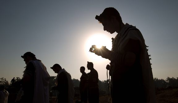 Israeli soldiers read from a holy book as they pray in a staging area near the Gaza border in southern Israel on Nov. 20, 2012. Israeli aircraft battered the headquarters of the Islamic National Bank, which Gaza&#39;s Hamas leaders set up to sidestep international sanctions on their rule. (Associated Press)