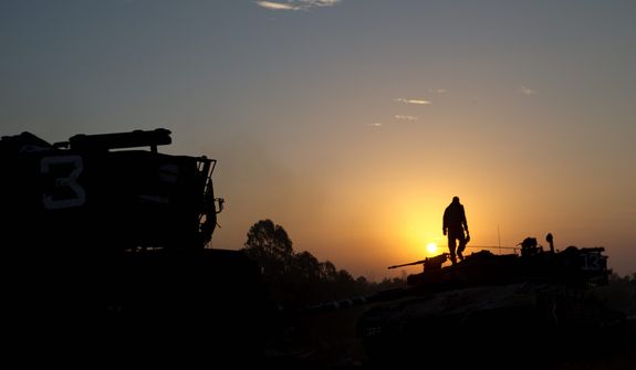 An Israeli soldier stands atop a military vehicle as the sun rises in a staging area near the Gaza border in southern Israel on Nov. 20, 2012. Israeli aircraft battered the headquarters of the Islamic National Bank, which Gaza&#39;s Hamas leaders set up to sidestep international sanctions on their rule. (Associated Press)