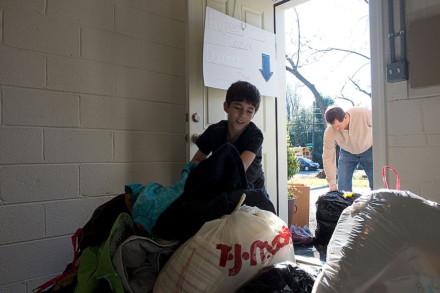 Nine-year-old Andrew Audas carries newly donated bags into the basement of his Bethesda, Md. home while his dad, Jim, gets more bags from outside. Their house has become the home base for the family's "Project Keep Them Cozy." The Audas children were struck by the devastation caused by Hurricane Sandy and told their parents they wanted to do something to help. So they created "Project Keep Them Cozy" and asked friends, schoolmates and neighbors to donate hats, gloves, coats and scarves. They have received all kinds of clothing, blankets and bedding, which they will drive up to New Jersey. They plan to stay up there through the Thanksgiving holiday to volunteer. This image was made Tuesday, Nov. 13, 2012. (Barbara L. Salisbury/The Washington Times)