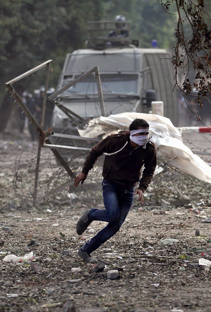 An Egyptian protester runs for cover during clashes with security forces near Tahrir Square in Cairo on Tuesday, Nov. 27, 2012. Demonstrators and police clashed just hours ahead of a planned mass rally by opponents of the country's Islamist president, who are demanding he rescind decrees that granted him near-absolute powers. (AP Photo/Khalil Hamra)
