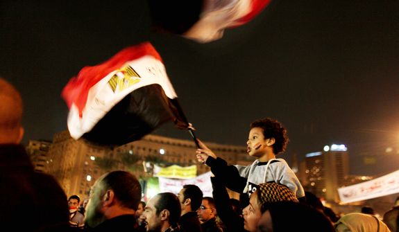 An Egyptian boy atop his mother’s shoulders waves a national flag in Tahrir Square in Cairo, where several hundred demonstrators have been camping for two weeks. (Associated Press)