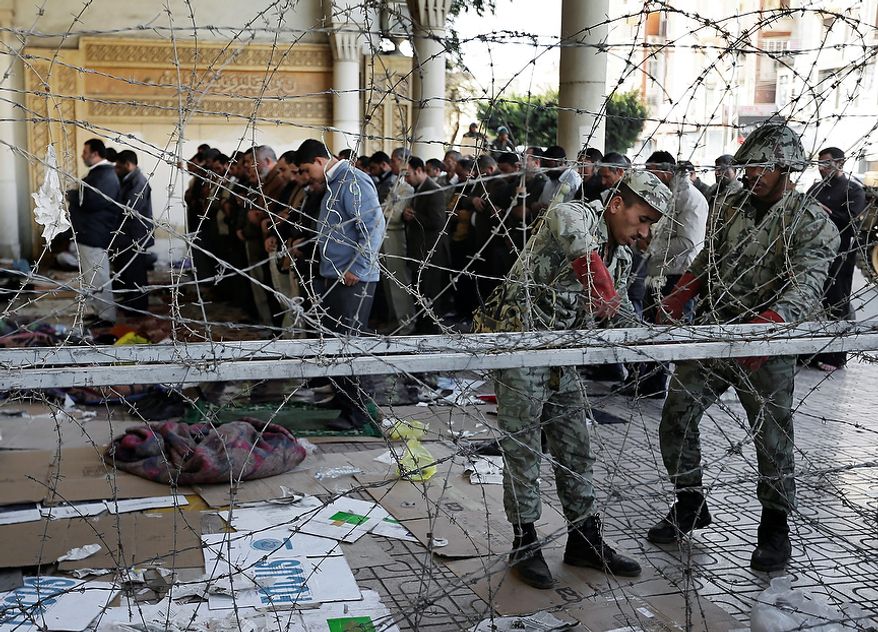 Army soldiers install barbed wire Dec. 6, 2012, near the presidential palace in Cairo to secure the site of overnight clashes between supporters and opponents of President Mohammed Morsi, as supporters of Morsi pray. The Egyptian army has deployed tanks outside the presidential palace in Cairo following clashes between supporters and opponents of Morsi that left several people dead and hundreds wounded. (Associated Press)