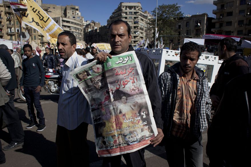 An Egyptian protester carries a copy of Al Wafd newspaper front page that reads in Arabic, "the brotherhood's crime, no legitimacy for a governor who is against his people," during a protest against President Mohammed Morsi near the presidential palace in Cairo on Dec. 7, 2012. (Associated Press)