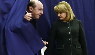 Romanian President Traian Basescu (left) exits a voting booth as his wife, Maria, stands by in Bucharest, Romania, on Sunday, Dec. 9, 2012. Millions of Romanians braved rain and snow as they went to the polls for a parliamentary election that center-left government is expected to win, but the result could lead to more of the political instability that has plagued the impoverished Balkan nation this year. (AP Photo)