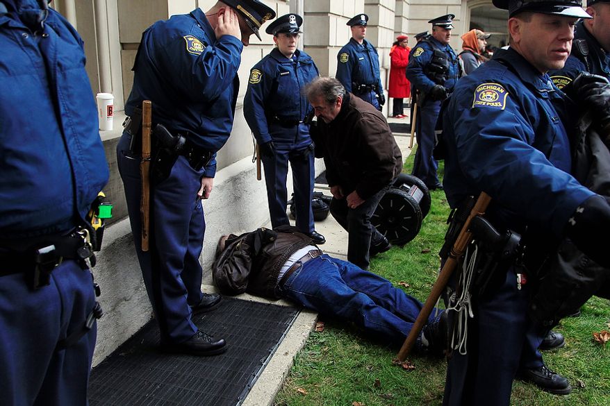 Michigan State Police surround a man who was allegedly knocked off his segway scooter by a sheriff deputy on horseback during a rally on the State Capitol grounds in Lansing, Mich., Tuesday, Dec. 11, 2012. The crowd is protesting right-to-work legislation that was passed by the state legislature last week. (AP Photo/Carlos Osorio)