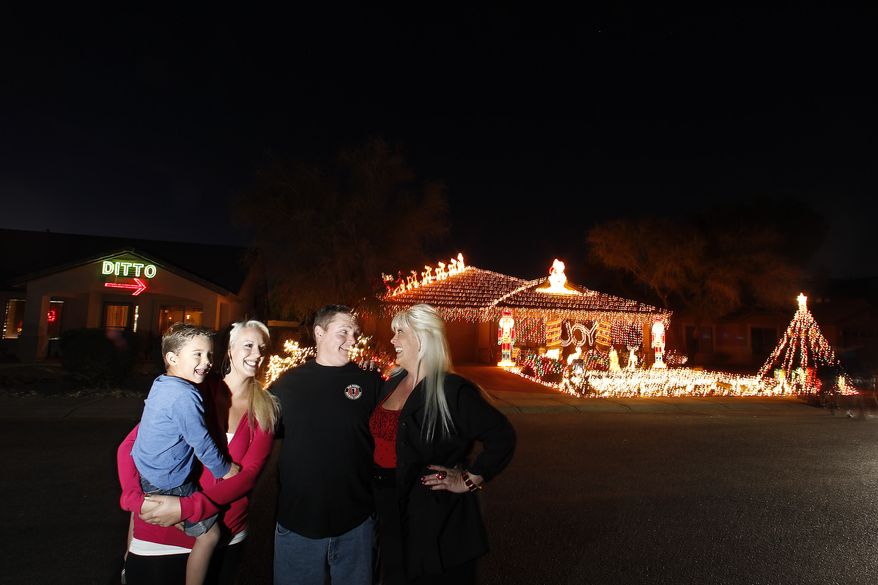 Kristina Green (right), her daughter Breanah Gray (second left) and grandson Cameron Gray (left) laugh together with neighbor Eric Cyr on Dec. 11, 2012,as they pose in front of their homes in Maricopa, Ariz. Green could not compete with Cyr's 20,000 Christmas lights on his home, so she has put up a 450 light display that says "DITTO" with an arrow pointing to Cyr's home. (Associated Press)