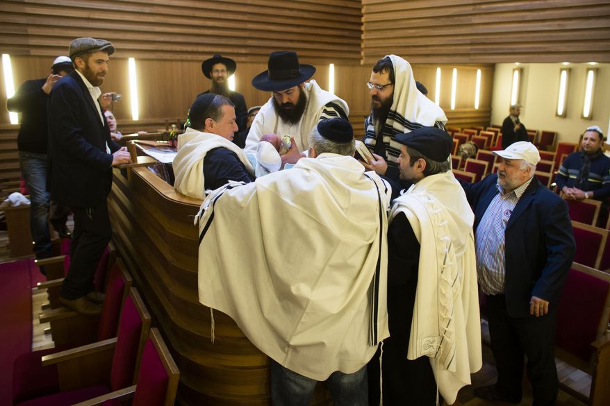 ** FILE ** Rabbi Yacov Gassinovitch (center), a mohel, is surround by other rabbis and relatives as he holds 8-day-old Jonathan during the boy's circumcision at synagogue in Berlin on Oct. 29, 2012. (Associated Press)