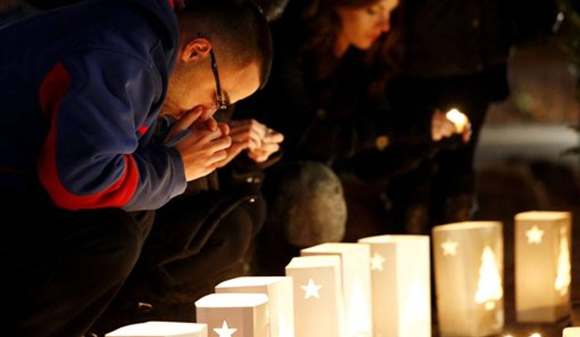 A man reacts placing candles on a makeshift memorial in honor of the victims who died a day earlier when a gunman opened fire in an elementary school, Saturday, Dec. 15, 2012, in Newtown, Conn. The man, who died from a self-inflicted wound, allegedly killed his mother at their home and then opened fire Friday inside the Sandy Hook Elementary school, massacring 26 people, including 20 children. (AP Photo/Julio Cortez)