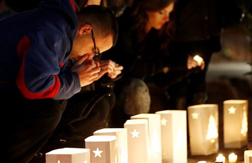 A man reacts placing candles on a makeshift memorial in honor of the victims who died a day earlier when a gunman opened fire in an elementary school, Saturday, Dec. 15, 2012, in Newtown, Conn. The man, who died from a self-inflicted wound, allegedly killed his mother at their home and then opened fire Friday inside the Sandy Hook Elementary school, massacring 26 people, including 20 children. (AP Photo/Julio Cortez)