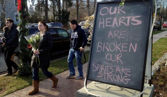 Jessica Henderson, 19, walks past a sign with a bouquet of flowers to lay at a memorial at the Sandy Hook School in Newtown, Conn., on Saturday, Dec. 15, 2012. The massacre of 26 children and adults at Sandy Hook Elementary school elicited horror and soul-searching around the world even as it raised more basic questions about why the gunman, 20-year-old Adam Lanza, would have been driven to such a crime and how he chose his victims. (AP Photo/Allen Breed)


