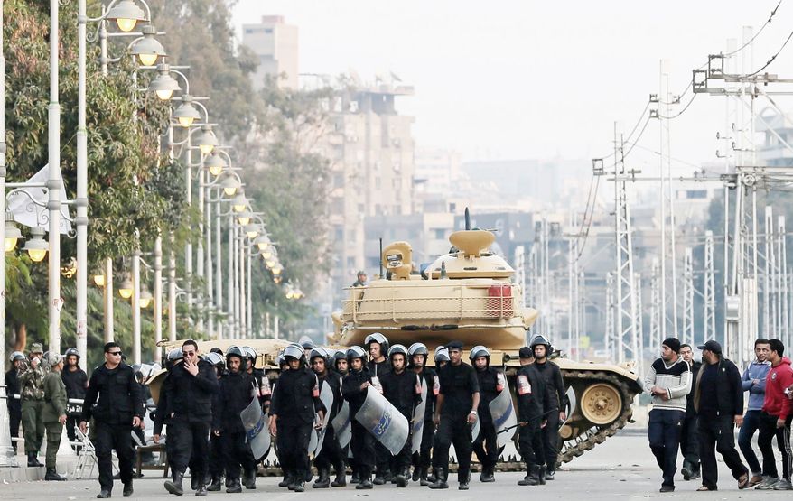 Egyptian riot police walk past a tank in Cairo on Sunday while one protester in Tahrir Square wears a sticker reading, “No to the supreme guide’s rule.” Egyptian rights groups say the country’s constitutional referendum was marred by violations. (Associated Press)