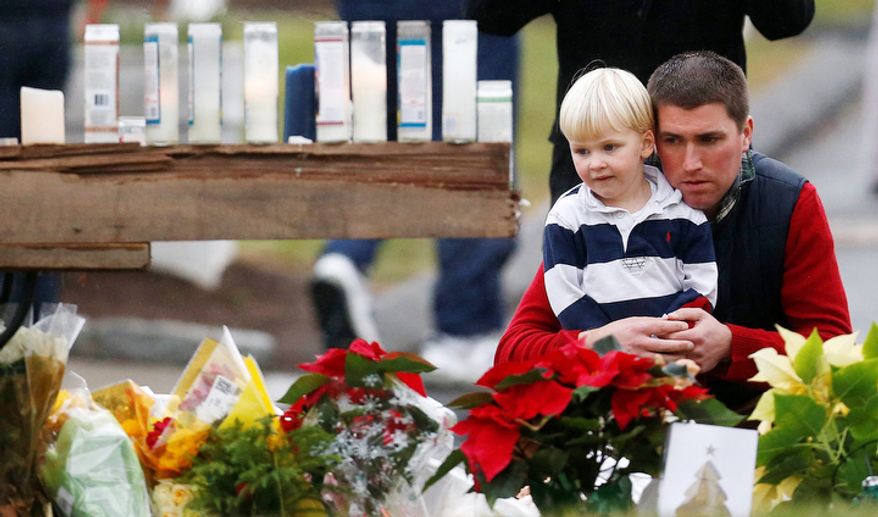A man holds a child while paying respects to shooting victims at a makeshift memorial outside of St. Rose of Lima Roman Catholic Church, Sunday, Dec. 16, 2012, in Newtown, Conn. (AP Photo/Julio Cortez)