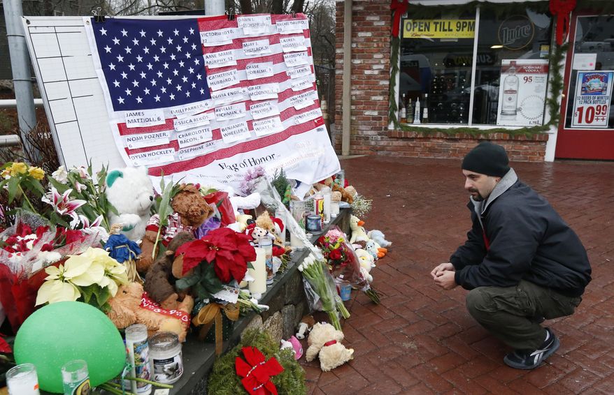 Mark Sorrentino of Naugatuck, Conn., pays his respects near a U.S. flag with the names of the school-shooting victims on a makeshift memorial in the Sandy Hook village of Newtown, Conn., on Monday, Dec. 17, 2012. (AP Photo/Julio Cortez)
