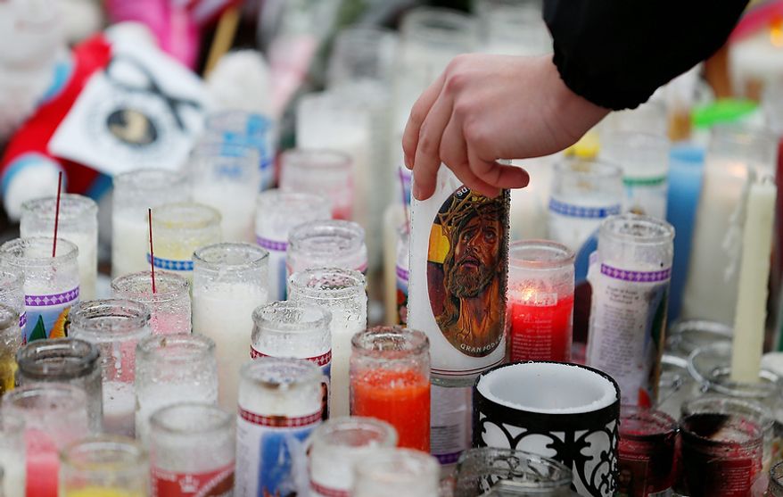 Ryan Bartolotta, 17, picks up a candle to drain out rainwater and light it on a makeshift memorial in the Sandy Hook village of Newtown, Conn., on Monday, Dec. 17, 2012, as the town mourns victims of the school shooting. (AP Photo/Julio Cortez)