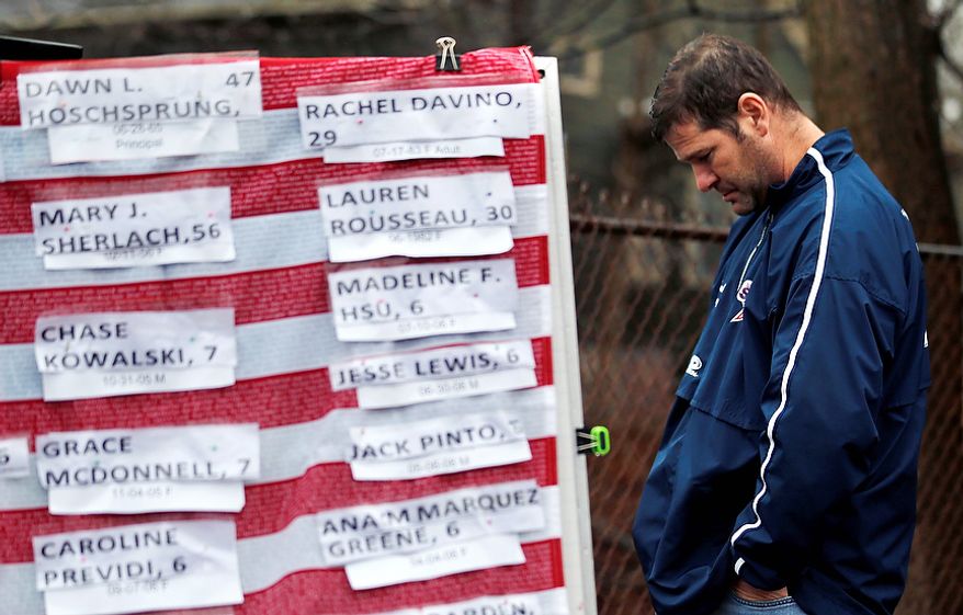A man pays his respects near a U.S. flag with the names of victims on a makeshift memorial in the Sandy Hook village of Newtown, Conn., on Monday, Dec. 17, 2012, as the town mourns victims of Friday's school shooting. (AP Photo/Julio Cortez)